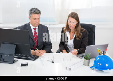 Due architetti insieme a discutere di blueprint alla scrivania in ufficio Foto Stock