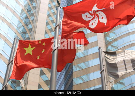 Cinese e Hong kong bandiere soffiare il vento con il palazzo di vetro sullo sfondo Foto Stock