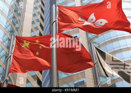 Cinese e Hong kong bandiere soffiare il vento con il palazzo di vetro sullo sfondo Foto Stock