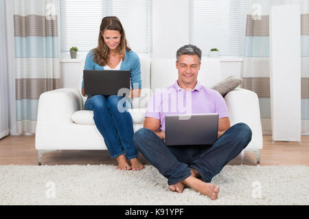 Coppia felice coppia utilizzando computer portatili in salotto Foto Stock