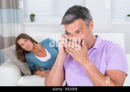 Donna matura guardando l'uomo a parlare in privato sul telefono cellulare Foto Stock