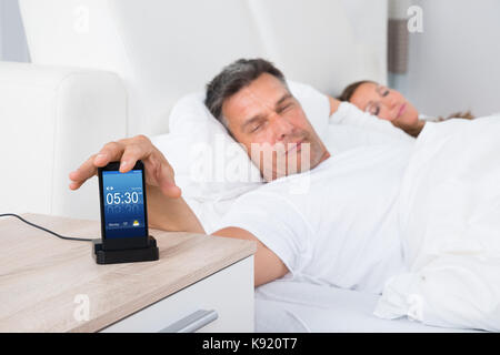 L'uomo sul letto del posticipo Sveglia sul telefono cellulare schermo durante il sonno Foto Stock