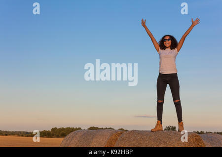 Outdoor ritratto della bella felice razza mista americano africano ragazza adolescente femmine giovane donna in piedi per celebrare a braccia alzate sorridente ridere wit Foto Stock