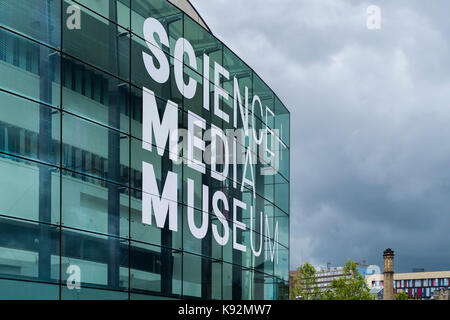 Grigio scuro sky & esterno della scienza e il Museo Multimediale (Bradford, West Yorkshire, Inghilterra, Regno Unito) - impressionante, curve, facciata vetrata & enorme nome sign. Foto Stock