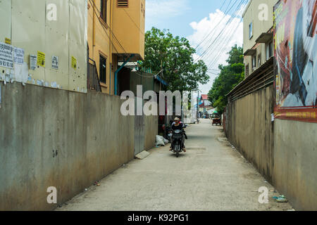 Tre passeggeri cavalcare una moto o bici, attraverso una tranquilla strada laterale a Phnom Penh. Una donna è la guida, mentre un bambino si siede nel mezzo. Foto Stock