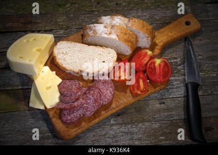 Salsiccia formaggio pomodoro pane giacciono su uno sfondo di legno Foto Stock