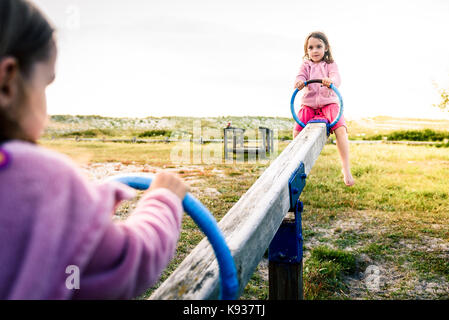 Poco due gemelle bambini stanno cavalcando altalena altalena nel parco. attivo dei bambini che giocano su teeter-tooter n un parco giochi in un parco in una giornata di sole. Foto Stock