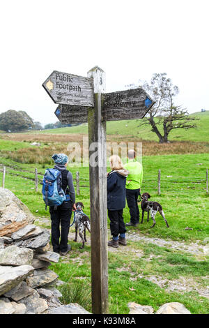 3 escursionisti e 2 tedesco dai capelli corti dei puntatori accanto a un cartello in legno post vicino Latterbarrow, Hawkshead, Lake District, Cumbria, England, Regno Unito Foto Stock