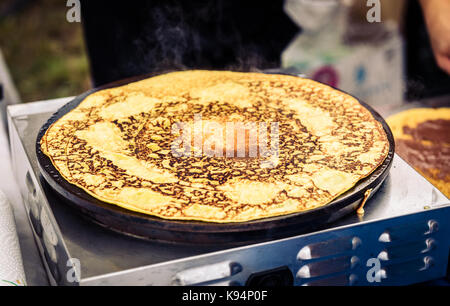 Realizzazione di Crepes Pancake nel mercato aperto festival fiera. una mano è rendere crepes all'aperto su una griglia metallica con bastone di legno su un outdoor summer fest Foto Stock