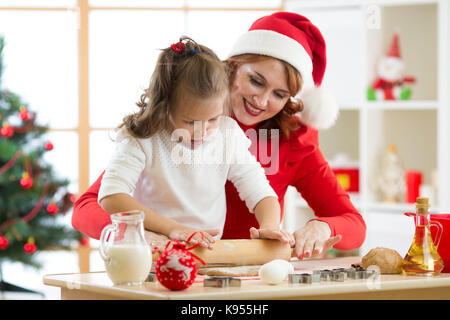 La famiglia la madre e il bambino rotolare la pasta, cuocere biscotti di Natale in festival sala decorata Foto Stock