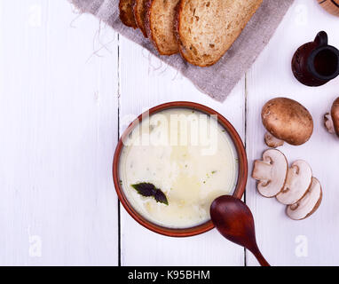 Spesso la zuppa cremosa con funghi in un round piastra di argilla su un bianco sullo sfondo di legno, vista dall'alto Foto Stock