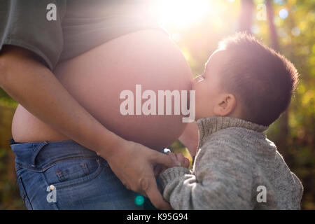 Bambino felice azienda ventre della donna incinta in foresta Foto Stock