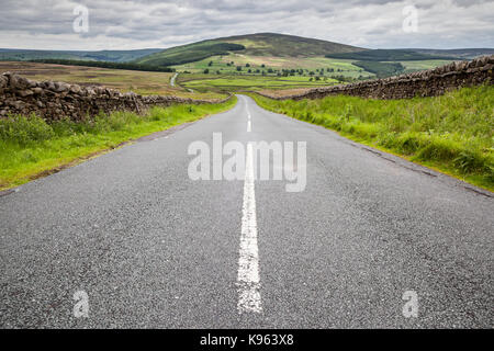 Una vista giù per una strada tortuosa nella campagna del Nord Yorkshire con muri in pietra a secco e un drammatico cielo nuvoloso. Foto Stock