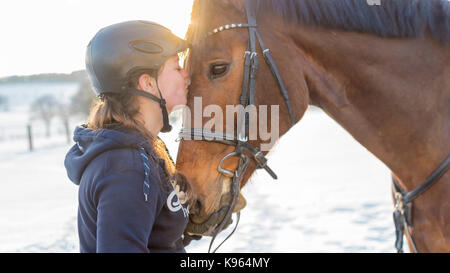 Donna rider baci hanoverian cavallo nella parte anteriore del paesaggio innevato Foto Stock