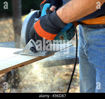 Chi detiene la sega circolare e taglia il legno compensato sul sito in costruzione. shot mostra le mani e il tool e segatura battenti. Foto Stock