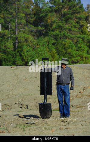 L uomo sta e legge un segno conformato come una grande pala presso il cratere dei diamanti è stato parco in murfreesboro, Arkansas. indossa jeans e un cappello. Foto Stock