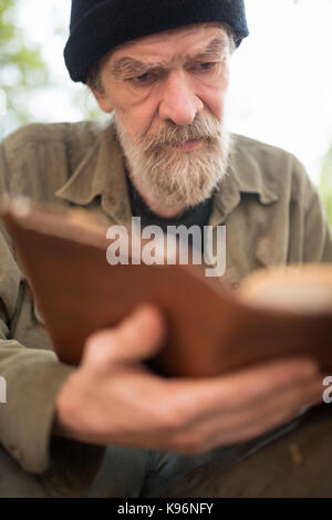 Close up ritratto di vecchio uomo beardy azienda prenota in mani. Foto Stock