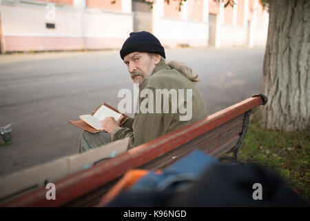 Vista posteriore del vecchio seduto su un banco di lavoro azienda prenota. Foto Stock