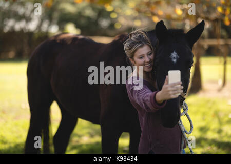 Felice giovane donna prendendo selfie con cavallo al granaio Foto Stock