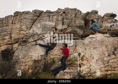 Gli amici di assistere l'uomo in arrampicata su roccia in una giornata di sole Foto Stock