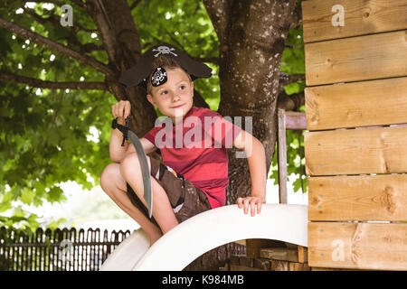 Carino ragazzo in costume pirata seduti sulla slitta nel parco giochi Foto Stock