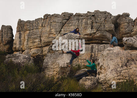 Gli amici di assistere l'uomo in arrampicata su roccia in una giornata di sole Foto Stock