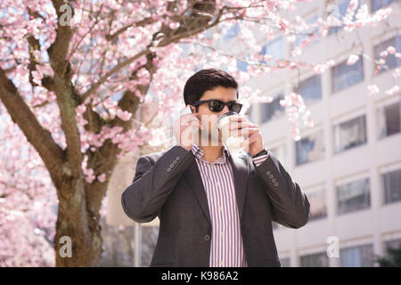 Imprenditore parlando al telefono cellulare mentre un caffè in posizione di parcheggio Foto Stock