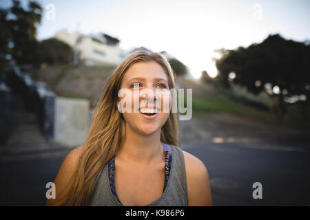 Allegro giovane donna che guarda lontano mentre permanente sulla strada contro sky Foto Stock