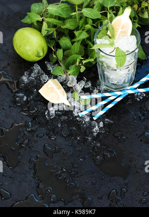 Il mojito set di cottura. mazzetto di menta fresca, calce, scaglie di ghiaccio e di cocktail bicchiere in ardesia nera sullo sfondo di pietra Foto Stock