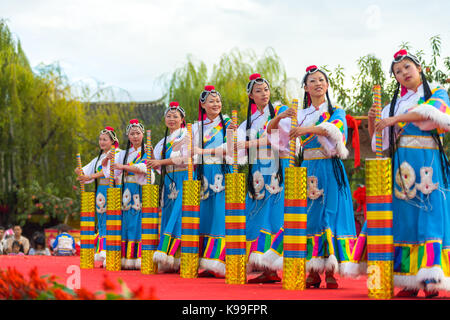 Lijiang, Cina - 2 Ottobre 2007: la minoranza etnica donne vestiti in abiti tradizionali danze sul palcoscenico usando un palo e contenitore nella città vecchia di Lijiang Foto Stock