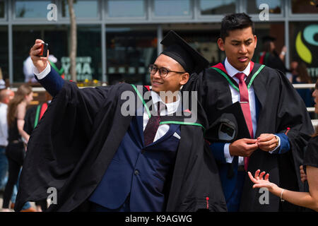 Istruzione superiore nel Regno Unito: un gruppo di stranieri asiatici oltremare Aberystwyth studenti universitari indossando accademici tradizionali abiti e schede di mortaio di prendere una fotografia selfie sul loro giorno di graduazione, Luglio 2017 Foto Stock