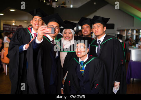 Istruzione superiore nel Regno Unito: un gruppo di stranieri asiatici oltremare Aberystwyth studenti universitari indossando accademici tradizionali abiti e schede di mortaio di prendere una fotografia selfie sul loro giorno di graduazione, Luglio 2017 Foto Stock