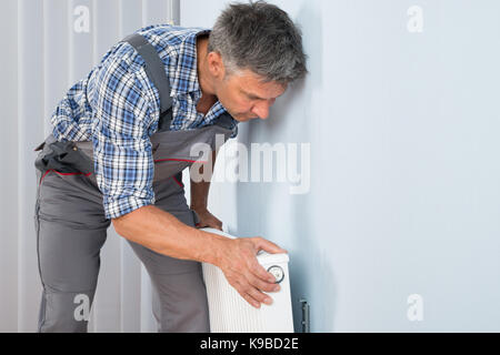 Ritratto di idraulico maschio che fissa il radiatore sulla parete Foto Stock