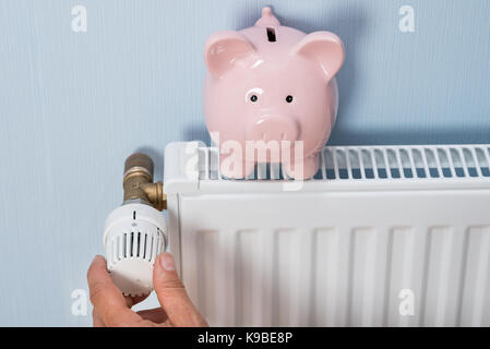 Close-up di man mano del termostato di regolazione con il salvadanaio sul radiatore Foto Stock