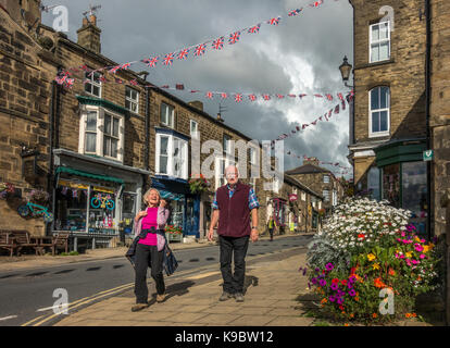 Due adulti maturi (70-80) a piedi il colorato ad alta via del ponte Pateley città mercato con bunting infilate in tutta la strada, North Yorkshire, Regno Unito Foto Stock