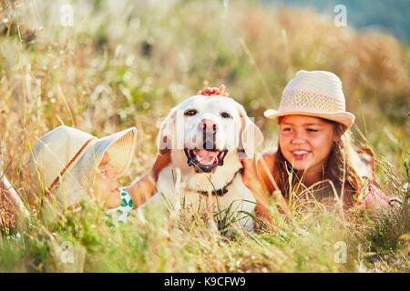Summertime in campagna. Le due ragazze giacente in erba abbraccio il cane (labrador retriever). Foto Stock