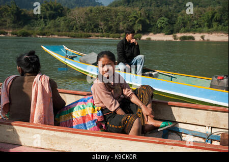 Una giovane ragazza laotiana si siede in un fiume in canoa con le montagne alle spalle in Muang Ngoi Laos Foto Stock