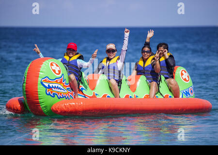 Donne filippino cavalcare un drago banana boat nel verde isola il passaggio off Spiaggia Bianca in Puerto Galera, Oriental Mindoro Island, Filippine. Foto Stock