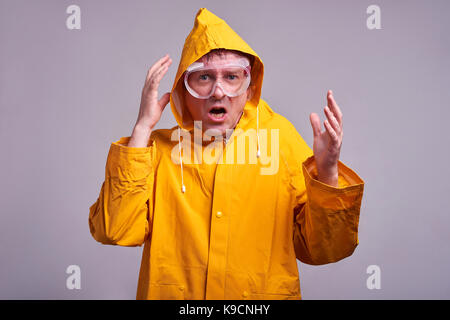 Un uomo di mezza età in un impermeabile giallo e occhiali di sicurezza spaventati Foto Stock