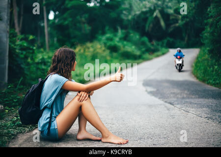 Giovane donna bella autostop seduti sulla strada a piedi scalzi. concetto di viaggio Foto Stock