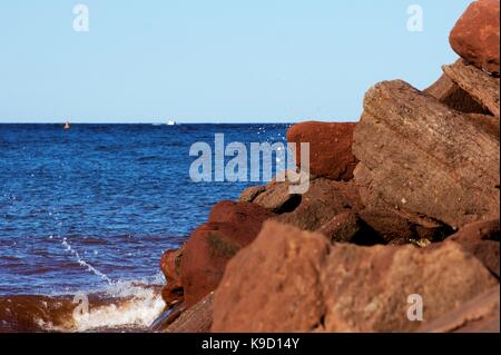 Rottura dell'onda su roccia con la barca e la boa in background Foto Stock