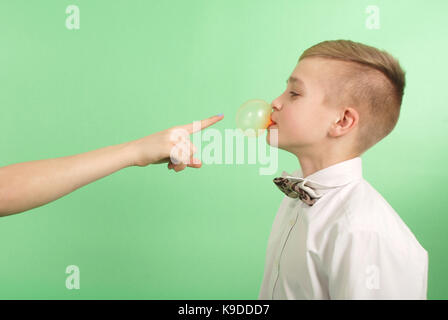 Ragazzo giovane stiramento da gomma da masticare che egli porta nella sua bocca isolati su sfondo verde Foto Stock