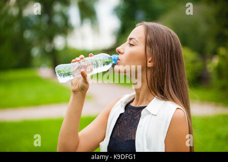 Ritratto di giovane bella dai capelli scuri donna acqua potabile ad estate parco verde Foto Stock