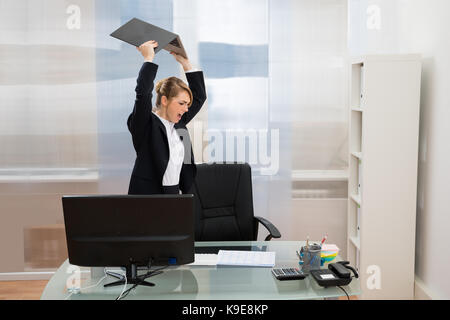 Arrabbiato imprenditrice permanente al desk gettando portatile in ufficio Foto Stock