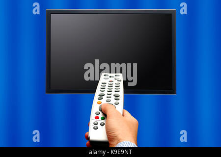 Maschio lato tenendo un telecomando puntato un schermo tv Foto Stock