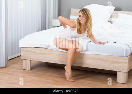 Donna seduta sul letto che soffrono di dolori alla schiena Foto Stock