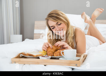 Giovane donna giaceva sul letto avente la prima colazione Foto Stock