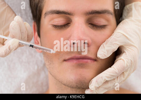 Close-up di dottore in guanto dando iniezione sul volto dell'uomo in clinica Foto Stock