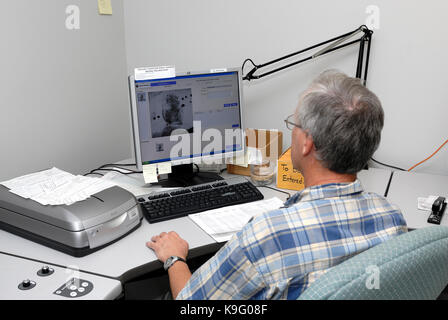 Male fingerprint technician sitting, classifying and identifying and analyzing fingerprints at a desk in a law enforcement facility. Foto Stock