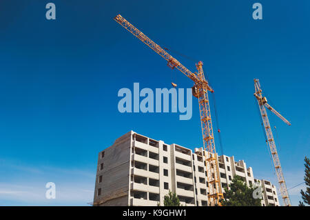 Alta yellow crane a costruire una casa nella bellissima luminoso cielo blu con nuvole. lavoratori nell'edificio in costruzione è la costruzione di una casa. Foto Stock
